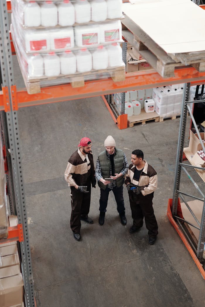 services-05 Three warehouse workers discuss logistics in an industrial storage facility.