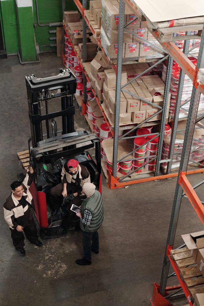 who-we-are High-angle view of warehouse employees operating a forklift surrounded by stacked shelves.