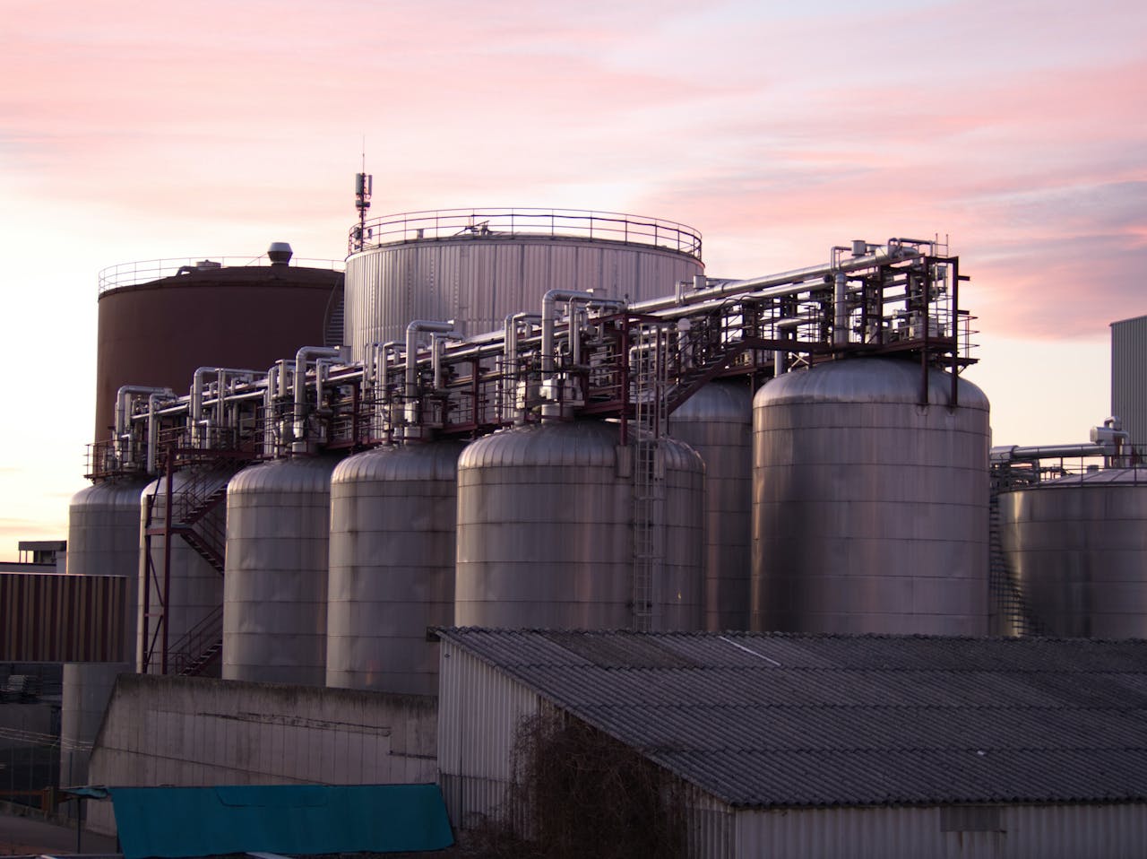about-bg A refinery with large stainless steel storage tanks during sunset, showcasing industrial infrastructure.